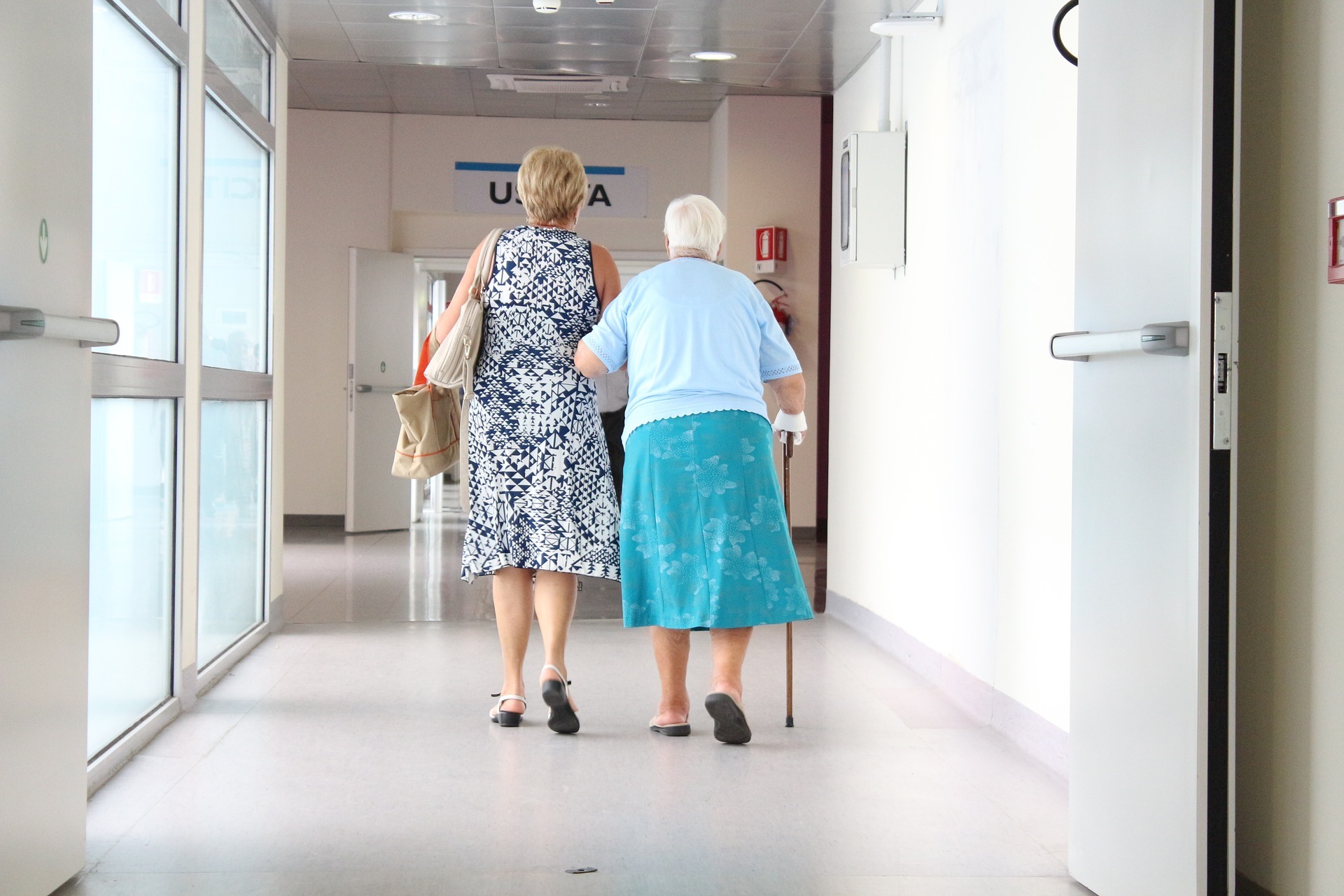 Two women walk, linking arms, down a hospital corridaor 